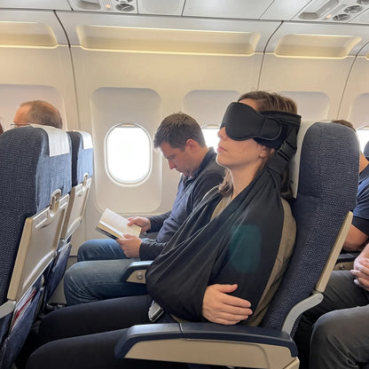 Woman asleep in a full economy cabin with the Travel Sleep Set, head held at the headrest