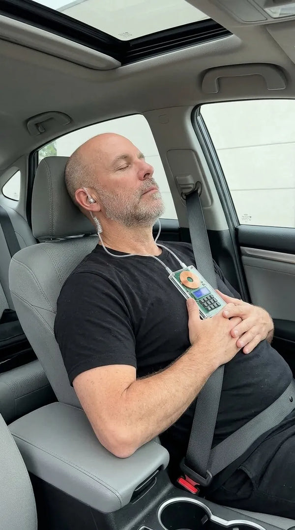 Man resting in the passenger seat of a car with Restwaves air-tube earphones
